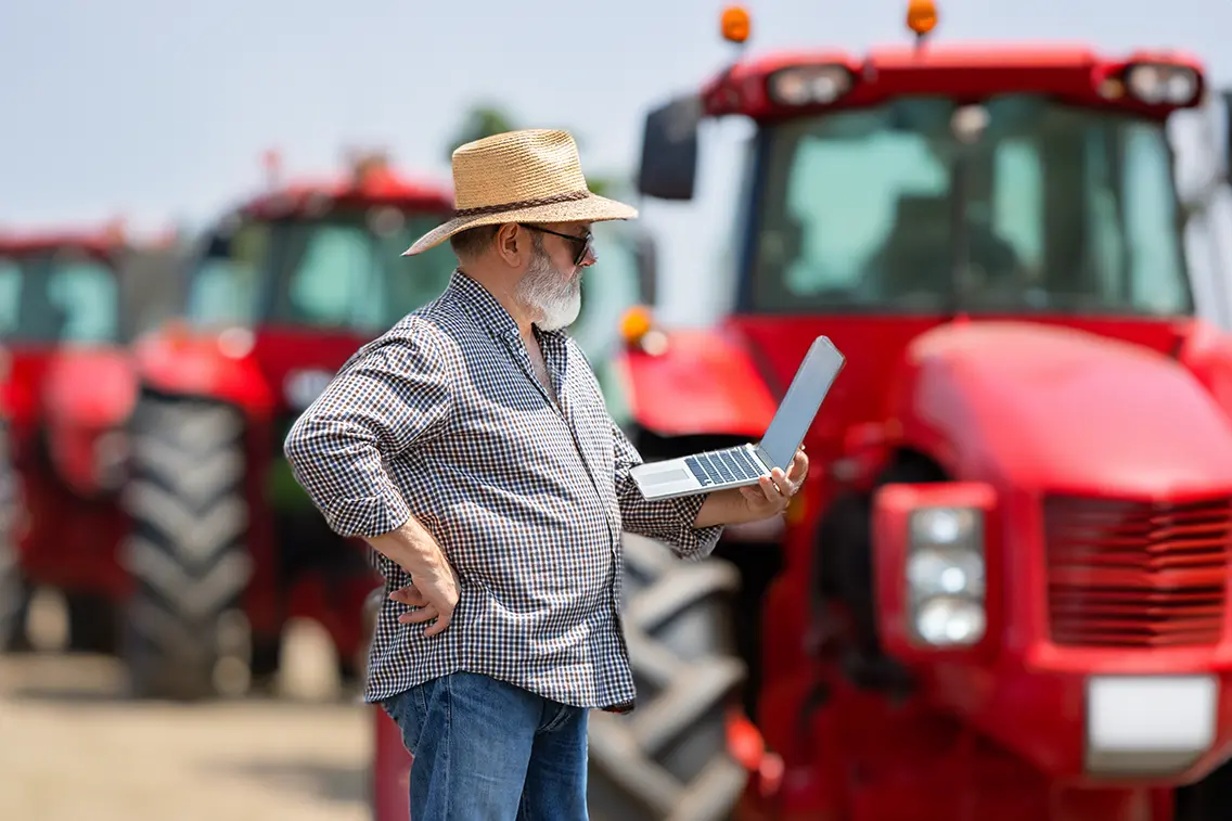 Farmer holding out a laptop in front of tractors