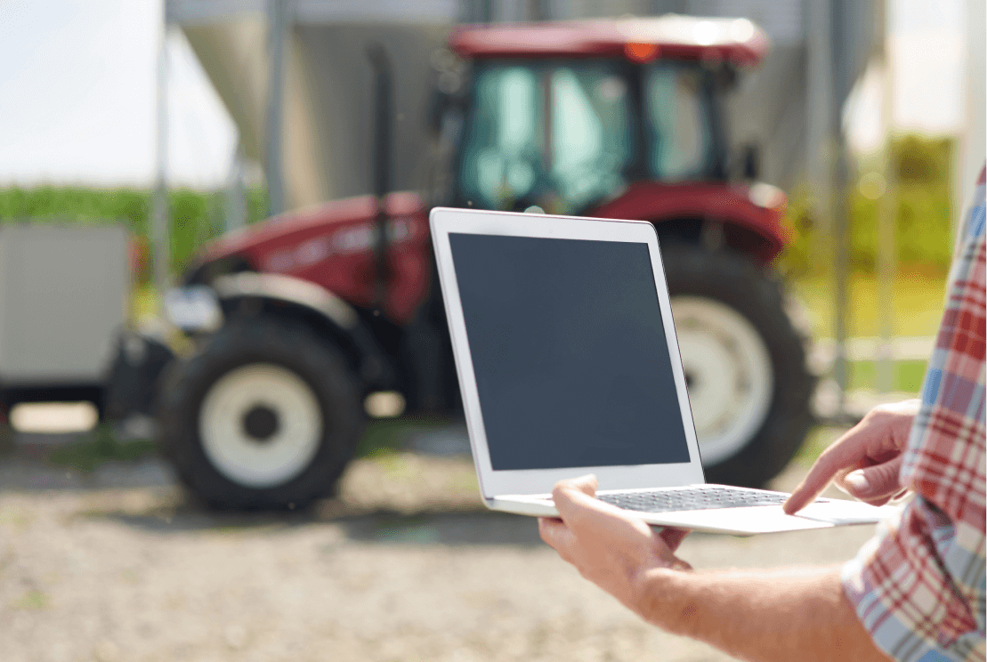 Image of person holding a laptop in front of a tractor